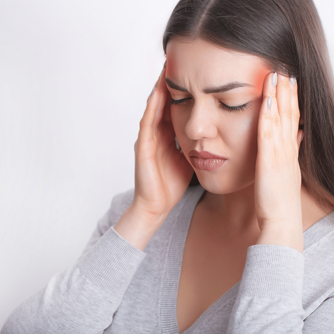Woman experiencing a headache, holding her temples in pain with visible tension in her facial expression.