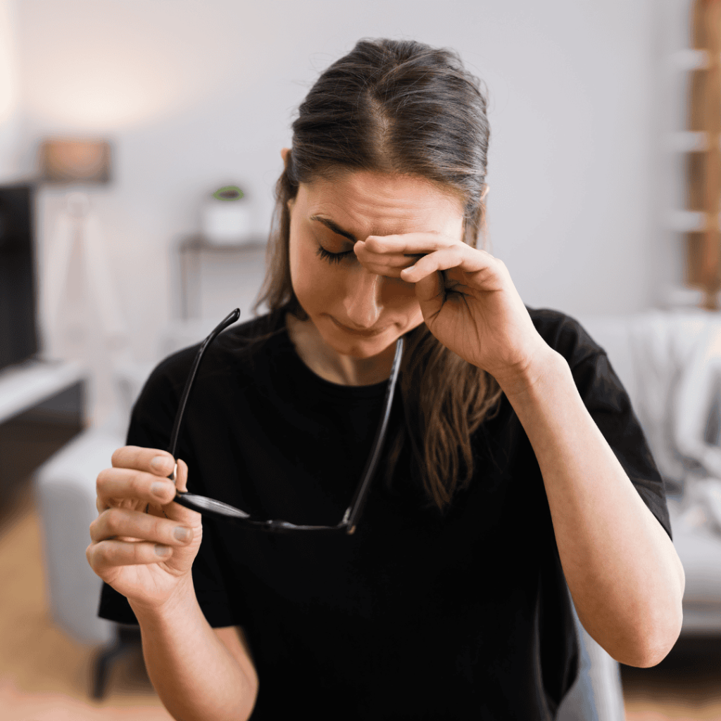 Woman taking off her glasses while checking her forehead with backside of hand in her living room.