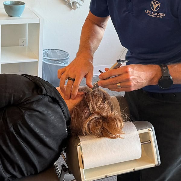 Chiropractor performing a precise neck adjustment using an activator tool on a patient lying face up at Life Aligned Wellness Center.