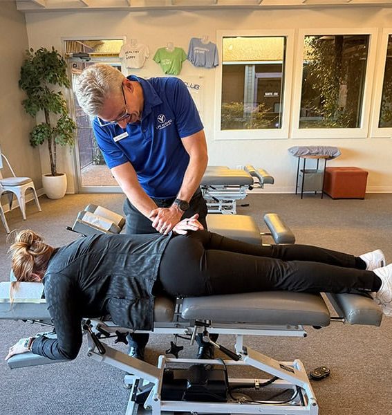 Dr. Cox performing a chiropractic adjustment on a patient lying face down on a treatment table in a modern clinic setting.