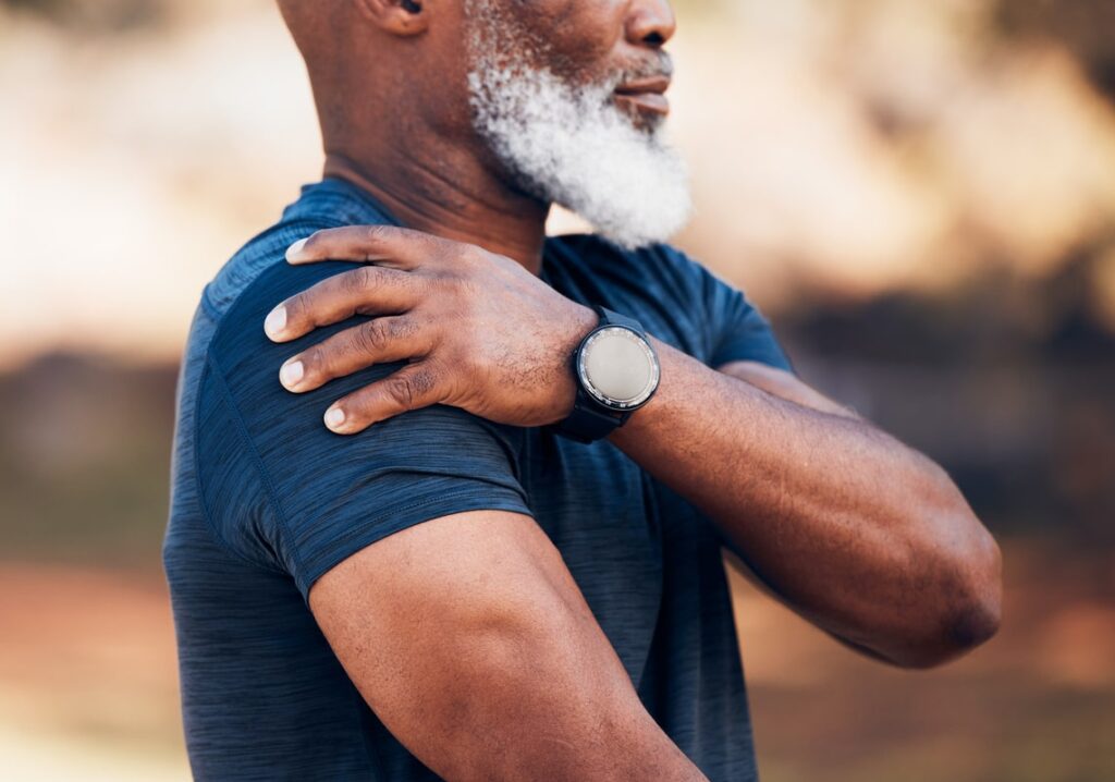 Older man in athletic wear holding his shoulder, showing signs of shoulder discomfort or joint pain.