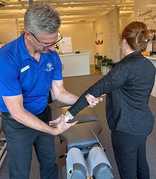 Chiropractor performing a manual arm and wrist adjustment on a standing female patient in a clinic setting, illustrating joint mobility treatment.