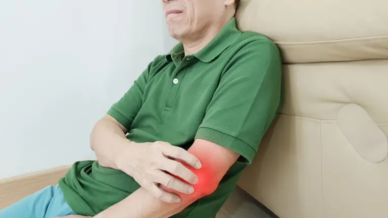 Man holding painful elbow showing symptoms of golfer’s elbow.