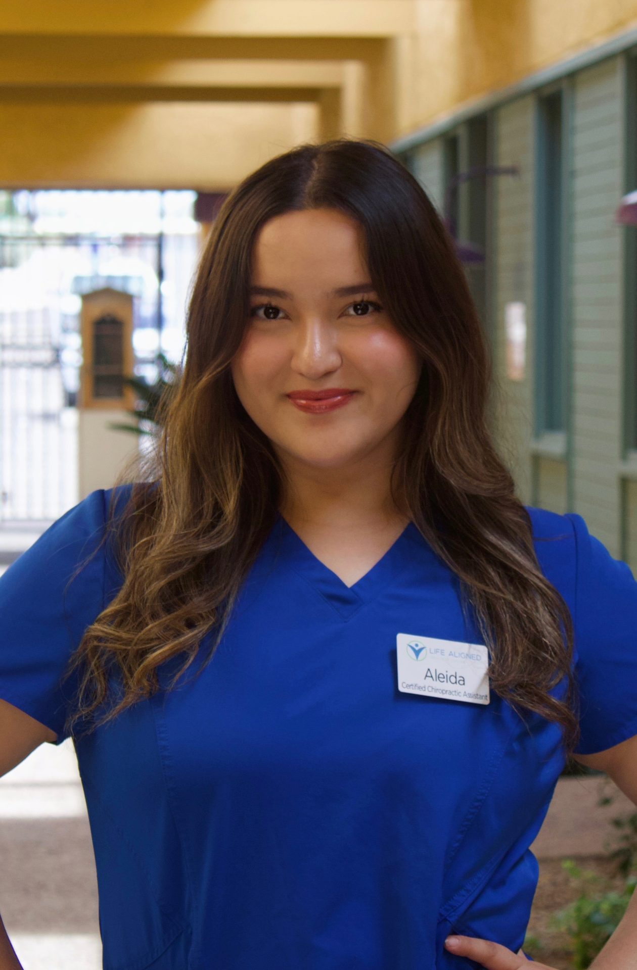Aleida, Chiropractic Case Manager, smiling warmly in blue scrubs at the clinic.